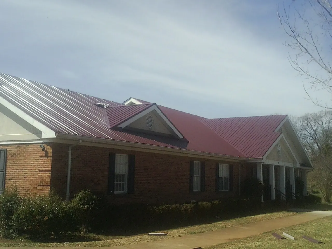 Red metal roof with gabled entries on a long brick building, from a Hail Damage Roof Repair job in Wellsburg
