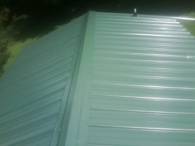 New green metal panels meeting at the ridge of a roof — Flat Roof Repair work by our crew in Wellsburg
