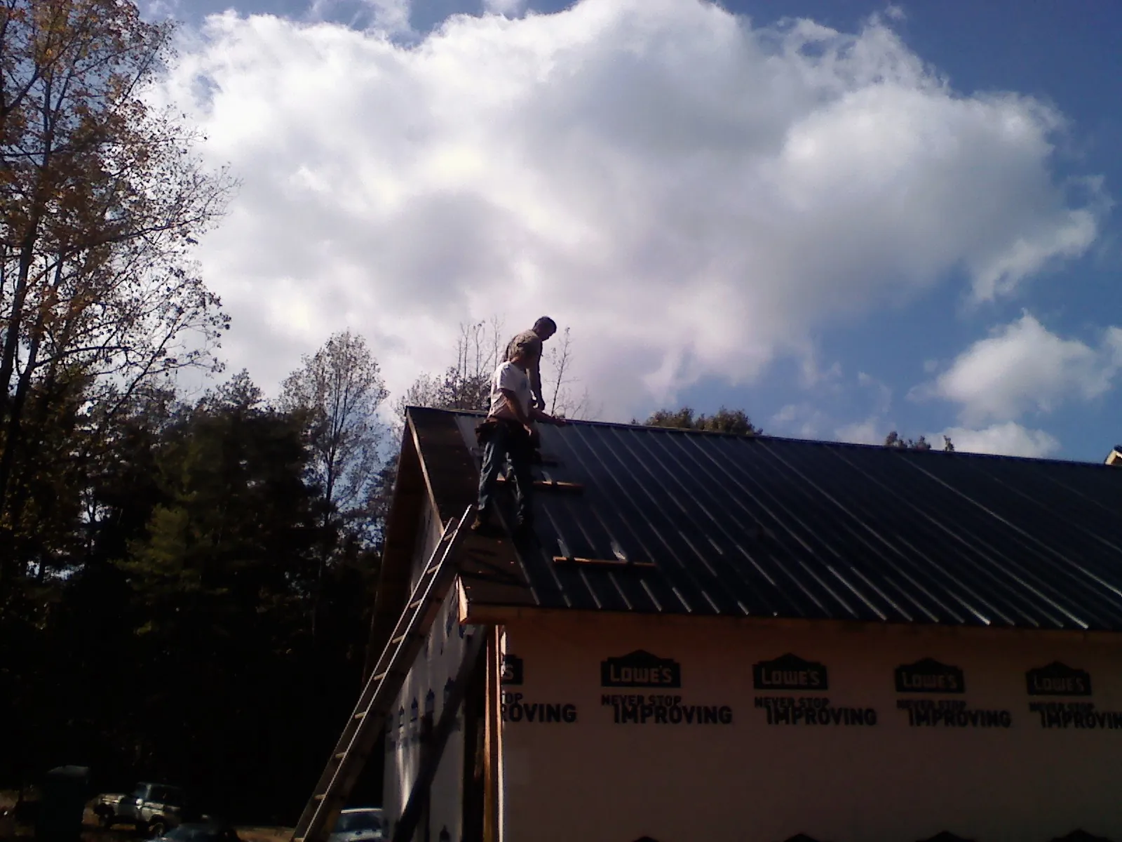 Roofer fastening dark metal panels high against a cloudy sky, from a Roof Inspection job in Wellsburg