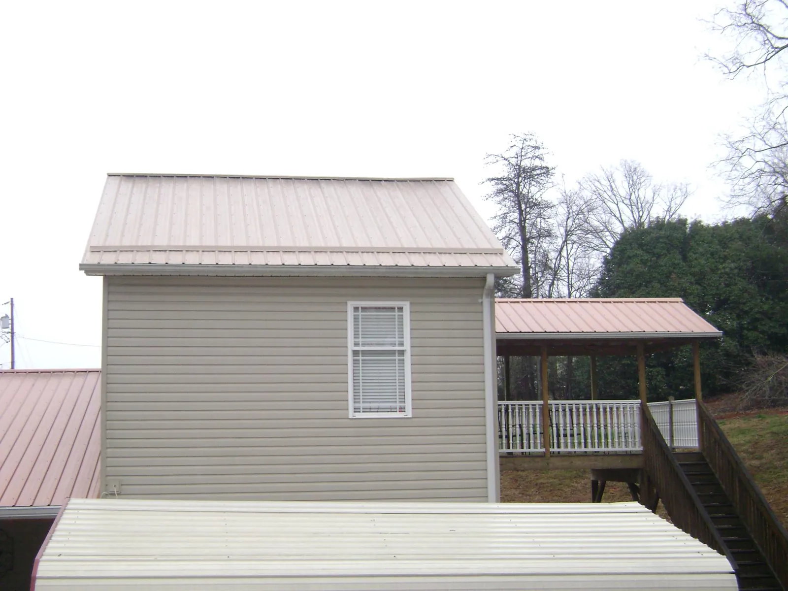 Tan metal roofs on a two story addition and attached porch, from a Roof Replacement job in Wellsburg